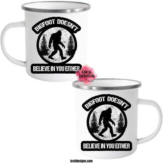 Bigfoot Coffee Mugs by KrcilDesigns.com | Graphic design on a white camp mug, featuring an all black graphic of a black silhouette of Bigfoot walking with black pine trees on both sides, above Bigfoot, text that reads: "BIGFOOT DOESN'T" in curved distressed bold block capital white letters, below, text that reads: "BELIEVE IN YOU EITHER" in distressed bold block capital white letters, all outlined in a thick bold black outline.
