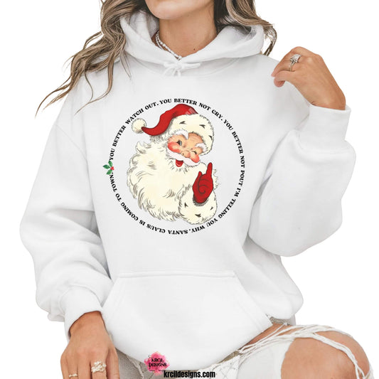 Christmas Sweaters by KrcilDesigns.com | Graphic design on a white hoodie, features a vintage-style Santa Claus with rosy cheeks, winking and pointing, with the iconic song lyrics to: "Santa Claus Is Coming To Town" wrapped around Santa in a circle, in bold black capital vintage Christmas letters with green holly and red berries.
