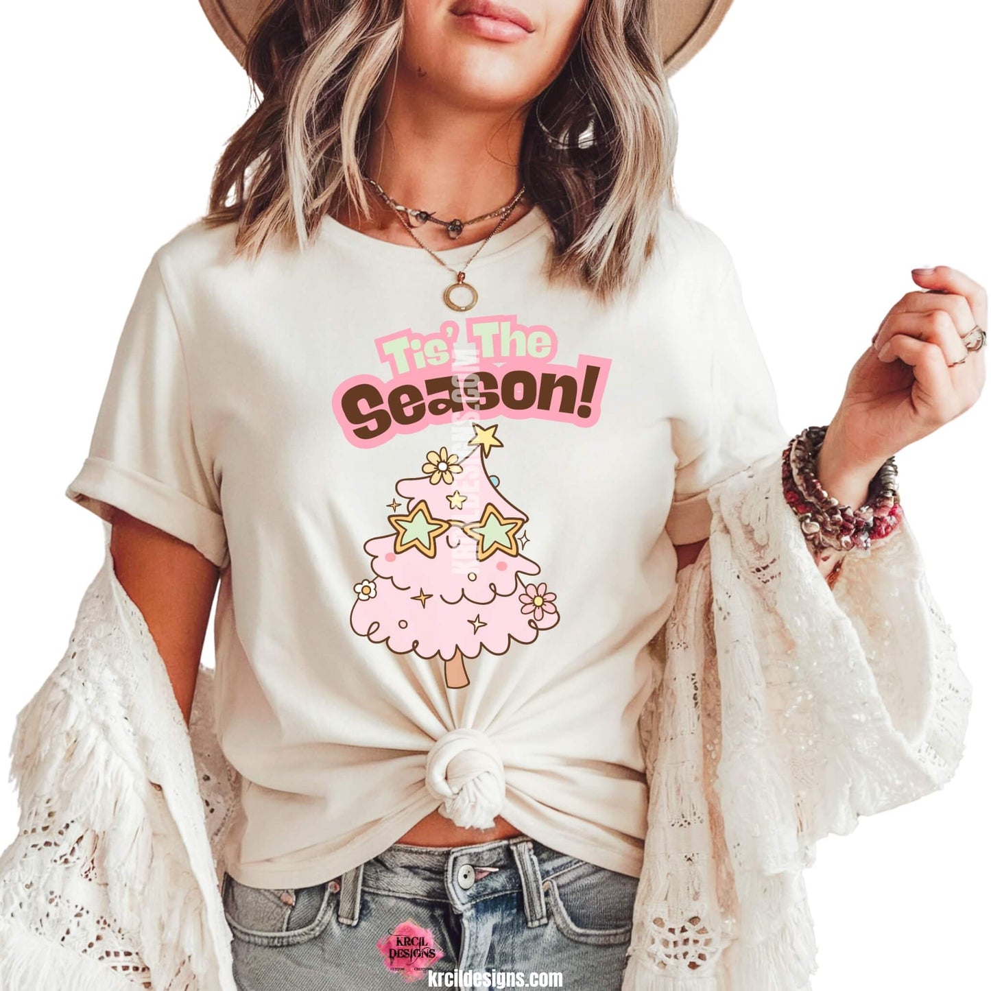 Christmas Tees by KrcilDesigns.com | Graphic design on a white t-shirt, features a cute pink Christmas tree wearing star-shaped sunglasses, decorated with pastel stars and pastel daisy flowers, with text that reads: "Tis' The Season!" in bold retro-style pink, green, and brown lettering curved above the tree.