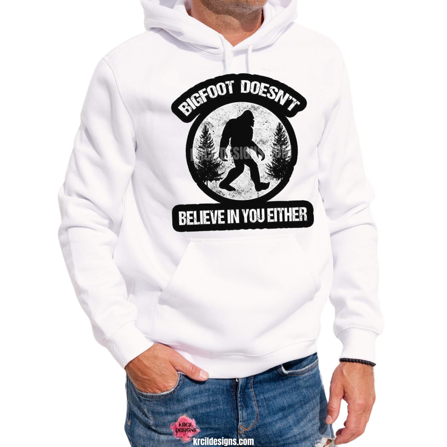 Bigfoot Shirts by KrcilDesigns.com | Graphic design on a white hoodie, featuring an all black graphic of a black silhouette of Bigfoot walking with black pine trees on both sides, above Bigfoot, text that reads: "BIGFOOT DOESN'T" in curved distressed bold block capital white letters, below, text that reads: "BELIEVE IN YOU EITHER" in distressed bold block capital white letters, all outlined in a thick bold black outline.