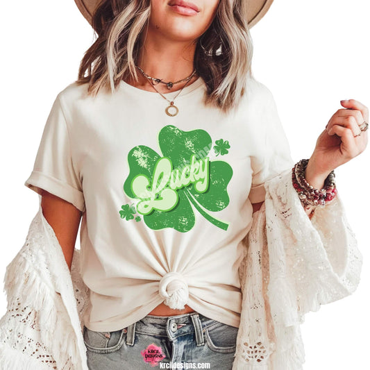 Distressed Retro Lucky Shamrock St. Patrick's Day T-Shirt by Krcil Designs | Make a fashion statement with our graphic tees t-shirts! Our buttery soft cozy tees will become your new weekend bestie! Get your green on this St. Patty's Day! Run your errands in style with our St. Patty's Day tote bag! Our graphics showcases the word Lucky in retro style green letters, outlined in two shades of green, placed on top of a shamrock and floating shamrocks on the sides. Shop Graphic Tees T-Shirts at KrcilDesigns.com