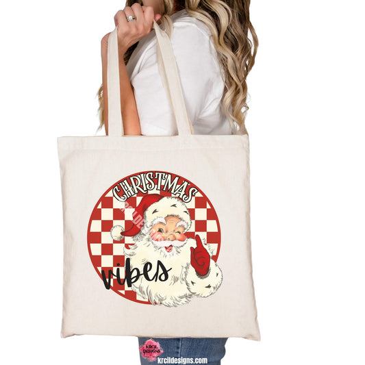 Christmas Tote Bags by KrcilDesigns.com | Graphic design on a canvas tote bag, features a vintage-style Santa Claus with rosy cheeks, winking and pointing, set against a red and white checkered circle background with text that reads: "Christmas Vibes" in bold cream vintage Christmas letters outlined in black.