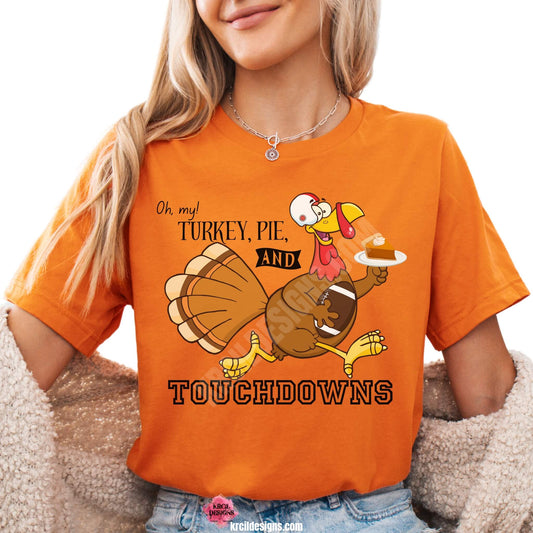 Funny Thanksgiving Shirts by KrcilDesigns.com | Graphic design on a orange t-shirt, featuring a cartoon turkey wearing a football helmet, holding a slice of pie topped with a dollop of whip cream on a white dinner plate, holding a football tucked under arm, and text that reads: "Oh, my! Turkey, Pie, and Touchdowns" in playful different fonts.