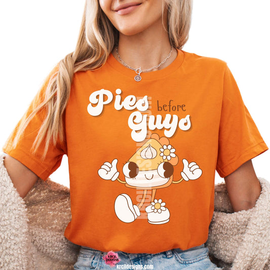 Funny Thanksgiving Shirts by KrcilDesigns.com | Graphic design on a orange t-shirt, featuring a playful cartoon piece of pumpkin pie retro character with arms, legs, and daisy flowers, striking a sassy pose with both hands making the 'thumbs up' sign. Surrounded by retro-style white text that reads: "Pies before Guys"