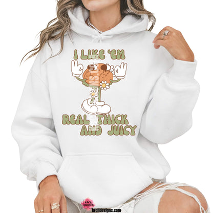 Funny Thanksgiving Shirts by KrcilDesigns.com | Graphic design on a white hoodie, featuring a playful cartoon turkey leg retro character with arms, legs, sunglasses, and daisy flowers, striking a sassy pose with both hands making the 'okay' sign. Surrounded by retro-style sage green text in all caps that reads: "I LIKE ‘EM REAL THICK AND JUICY"