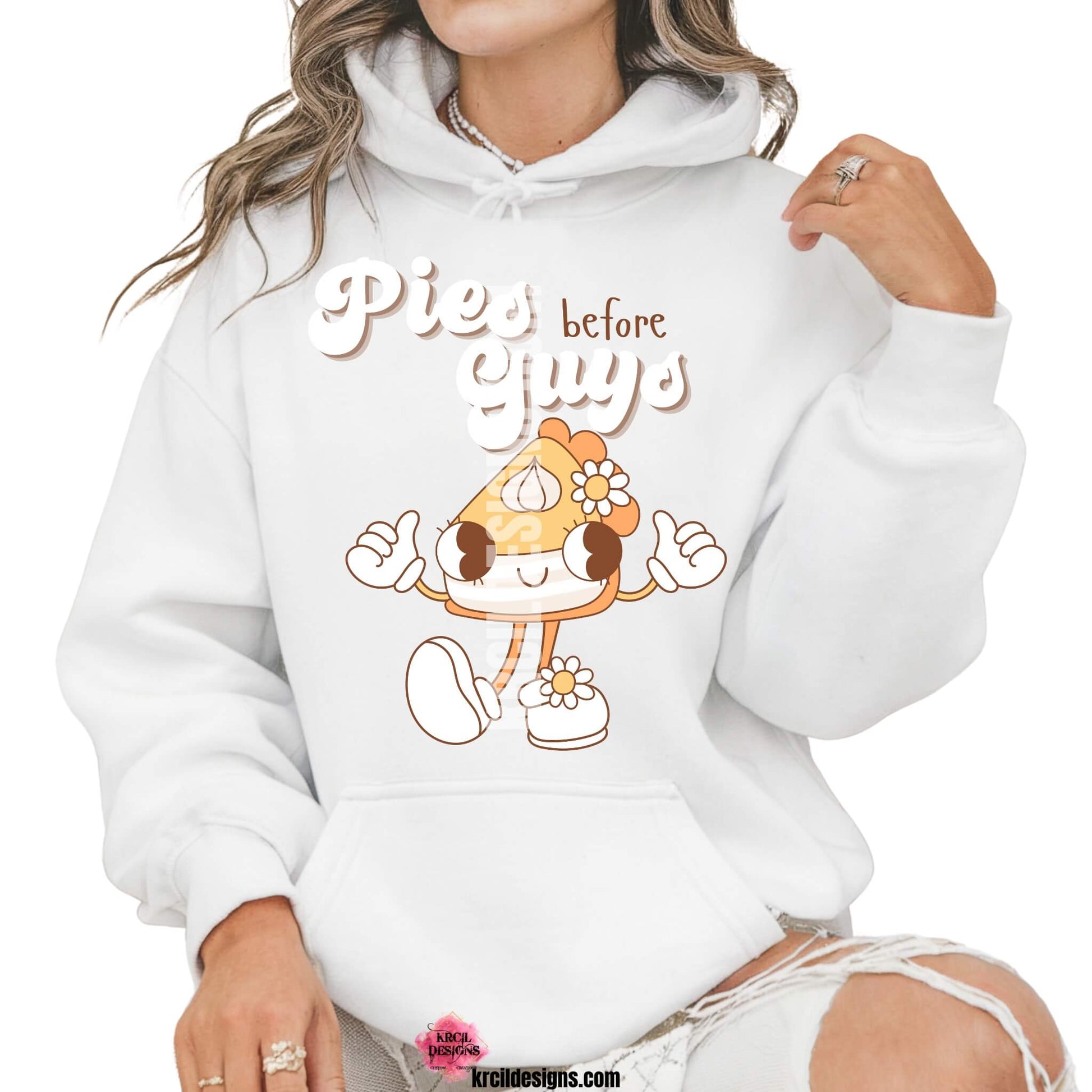 Funny Thanksgiving Shirts by KrcilDesigns.com | Graphic design on a white hoodie, featuring a playful cartoon piece of pumpkin pie retro character with arms, legs, and daisy flowers, striking a sassy pose with both hands making the 'thumbs up' sign. Surrounded by retro-style white text that reads: "Pies before Guys"