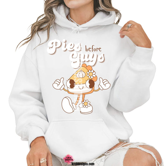 Funny Thanksgiving Shirts by KrcilDesigns.com | Graphic design on a white hoodie, featuring a playful cartoon piece of pumpkin pie retro character with arms, legs, and daisy flowers, striking a sassy pose with both hands making the 'thumbs up' sign. Surrounded by retro-style white text that reads: "Pies before Guys"