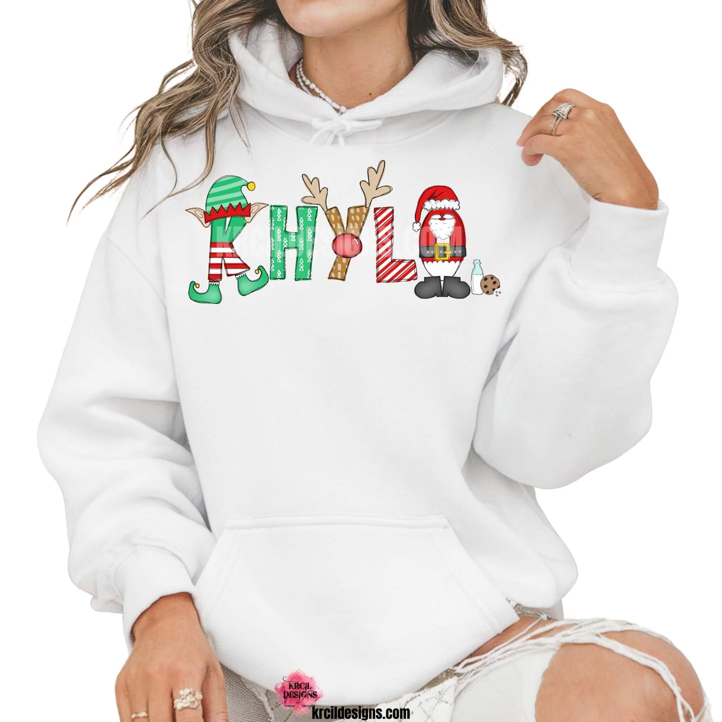 Christmas Personalized Name Shirts, Sweatshirts, Hoodies, by KrcilDesigns.com | Graphic Design on a white hoodie, features your name, in name style option: "Santa & Elf" where the designs of the letters are different festive Christmas patterns. The playful letters adorned with Santa, His Elf, Rudolph's Red Nose, Reindeer Antlers, and even Santa's Milk and Cookies.
