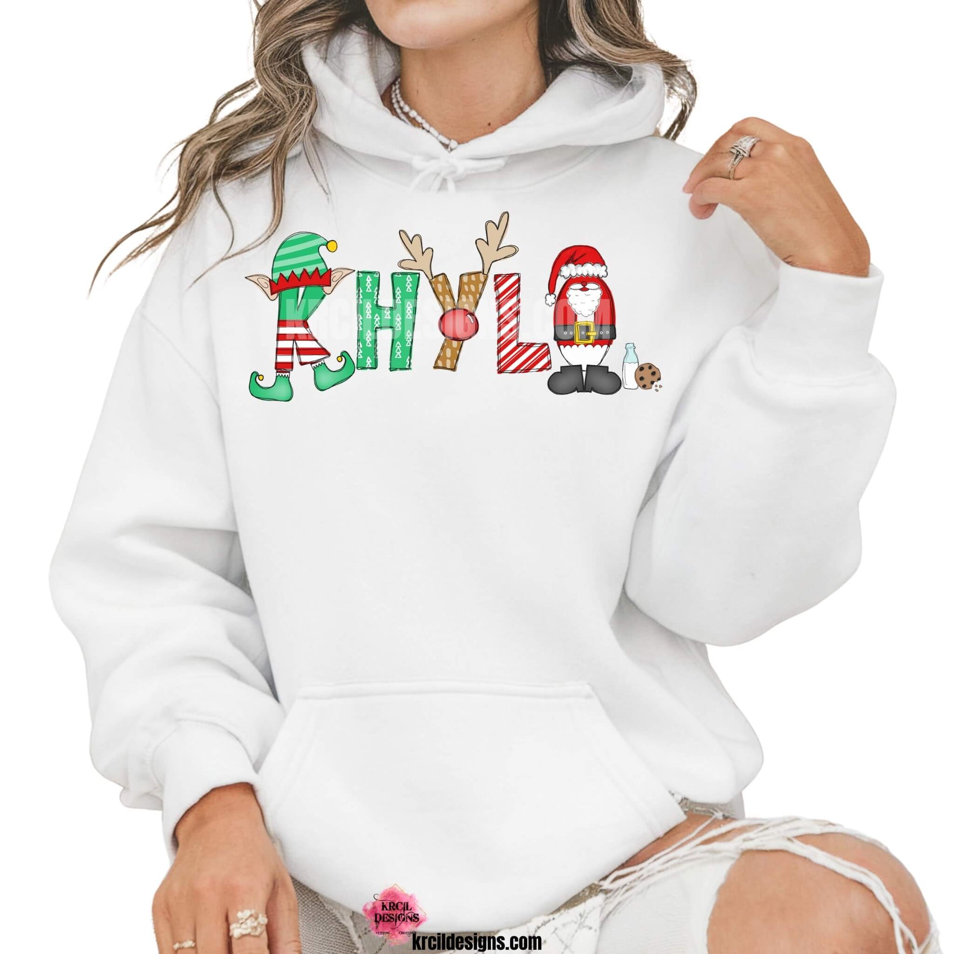 Christmas Personalized Name Shirts, Sweatshirts, Hoodies, by KrcilDesigns.com | Graphic Design on a white hoodie, features your name, in name style option: "Santa & Elf" where the designs of the letters are different festive Christmas patterns. The playful letters adorned with Santa, His Elf, Rudolph's Red Nose, Reindeer Antlers, and even Santa's Milk and Cookies.