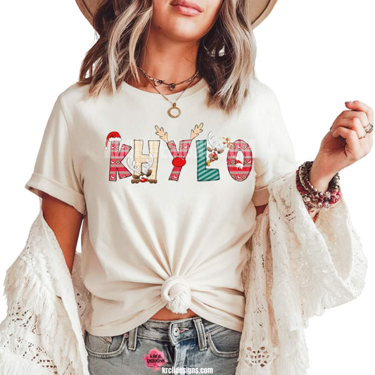 Christmas Personalized Name Shirts by KrcilDesigns.com | Graphic design on a white t-shirt, features your name, in name style option: "Christmas" where the designs of the letters are different festive Christmas patterns. The letters don a Santa Hat, Rudolph's Red Nose, and Reindeer Antlers. Santa and his Reindeer are playing Peek-a-Boo and are peeking out of letters.