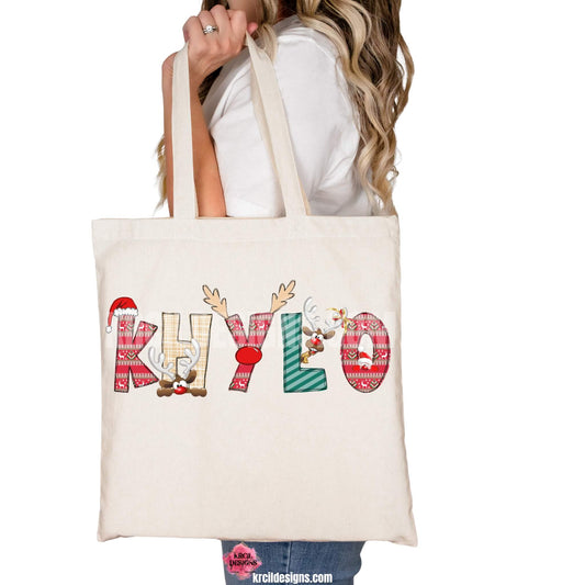 Christmas Personalized Tote Bags by KrcilDesigns.com | Graphic Design on a canvas tote bag, features your name, in name style option: "Christmas" where the designs of the letters are different festive Christmas patterns. The letters don a Santa Hat, Rudolph's Red Nose, and Reindeer Antlers. Santa and his Reindeer are playing Peek-a-Boo and are peeking out of letters.