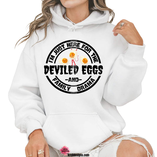 Sassy Sweatshirts and Hoodies by KrcilDesigns.com | Graphic design on a white hoodie, featuring a bold circular design and bold black text that reads: "I'm Just Here For The Deviled Eggs and Family Drama" with graphics of a devil deviled egg dressed up with a devil's tail, horns, and pitchfork, on each side are two deviled eggs.