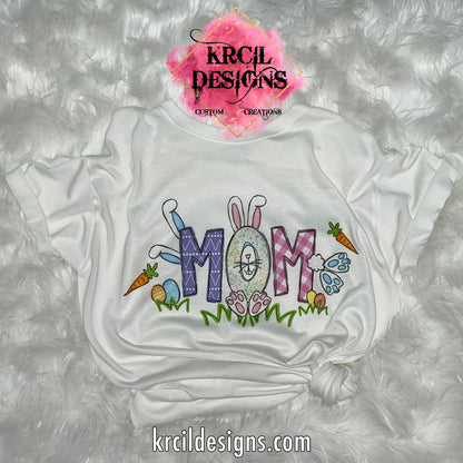 MOM | White | Your Name Easter T-Shirt by Krcil Designs | Our custom t-shirt, features your name, one lucky letter will be transformed into an adorable Easter bunny, while playful bunnies hop into the other letters. Surrounding the letters are colorful Easter eggs, carrots, and the letters atop a row of grass. Personalized T-Shirt—add the kids names and make it truly yours! This Easter, celebrate in style with matching family t-shirts—perfect for family photos! Shop Easter Shirts at KrcilDesigns.com