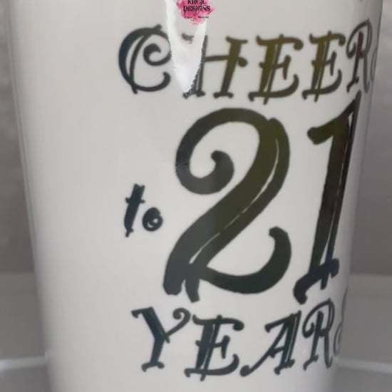 "Cheers to 21 Years" Shot Glass by Krcil Designs | Get ready to toast to the good times with our custom personalized shot glasses, perfect for the man cave. Pair them with your favorite bottle of liquor and put them in a basket for the ultimate gift. Don't forget to add the matching dish cloth tea towel set! Explore our sets and bundles options for gift ideas. Perfect for birthdays and holidays. Two toned, black interior, white exterior, ceramic shot glass. KrcilDesigns.com