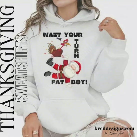 Funny Thanksgiving Shirts by KrcilDesigns.com | Graphic design on a white hoodie, featuring a cartoon Thanksgiving turkey wearing a pilgrim hat, stomping on Santa Claus, with playful motions and feathers flying. Bold black text in all caps, surrounds the scene, that reads: "WAIT YOUR TURN FAT BOY!" Fun holiday shirts that blend Thanksgiving and Christmas humor.