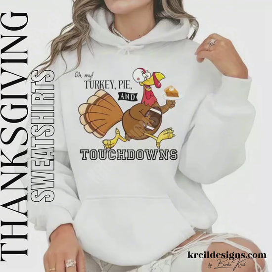 Funny Thanksgiving Shirts by KrcilDesigns.com | Graphic design on a white hoodie, featuring a cartoon turkey wearing a football helmet, holding a slice of pie topped with a dollop of whip cream on a white dinner plate, holding a football tucked under arm, and text that reads: "Oh, my! Turkey, Pie, and Touchdowns" in playful different fonts.