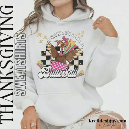 Funny Thanksgiving Shirts by KrcilDesigns.com | Graphic design on a white hoodie, featuring a fun Thanksgiving-themed design of a cartoon turkey swinging in on a disco ball in light pink and dark pink pattern, wearing a pink bow, surrounded by yellow stars, colorful retro stripes, and a black checkered background. Bold text above that reads: "I Came In Like A" with "Butterball" in large retro font below.