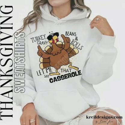 Funny Thanksgiving Shirts by KrcilDesigns.com | Graphic design on a white hoodie, featuring a cartoon turkey wearing sunglasses, the turkey is brown with a red wattle, yellow beak and feet, with yellow dots as a background. The words are scattered around the turkey in bold black text that reads: "Turkey Gravy Beans & Rolls LET ME SEE THAT CASSEROLE"